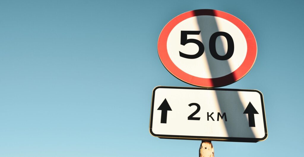 Clear speed limit and distance sign against blue sky, offering guidance and information.