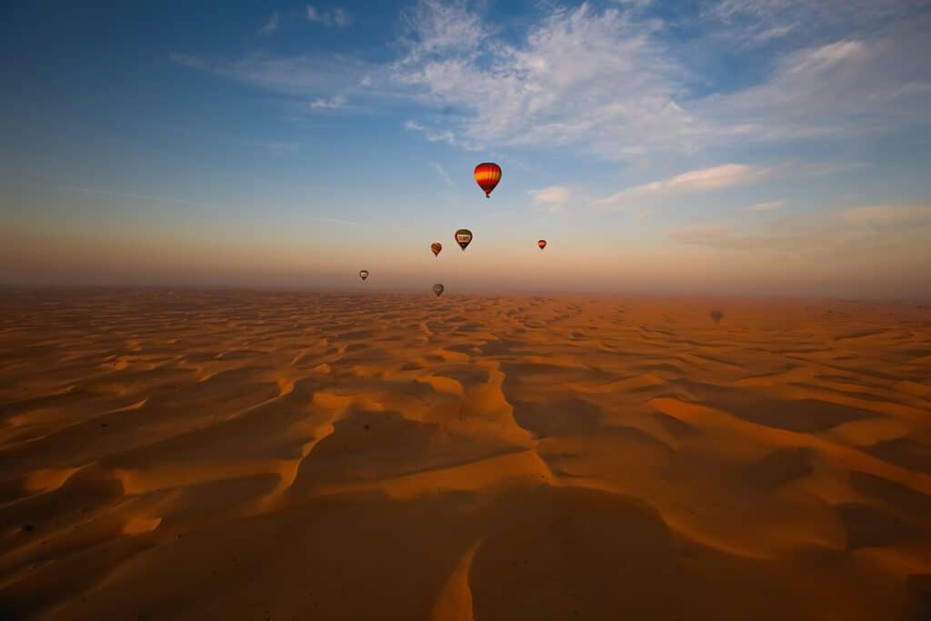 Stunning view of hot air balloons floating above the vast Dubai desert at dawn.